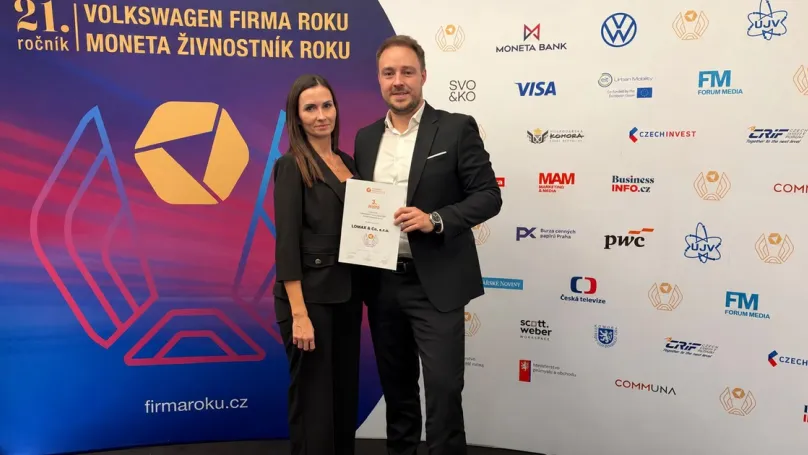 Two people holding the LOMAX certificate in front of the Firma roku 2026 event backdrop